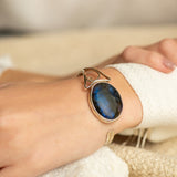 Brazalete artesanal de plata con gran piedra labradorita azul en muñeca femenina - Rocas & Cristales